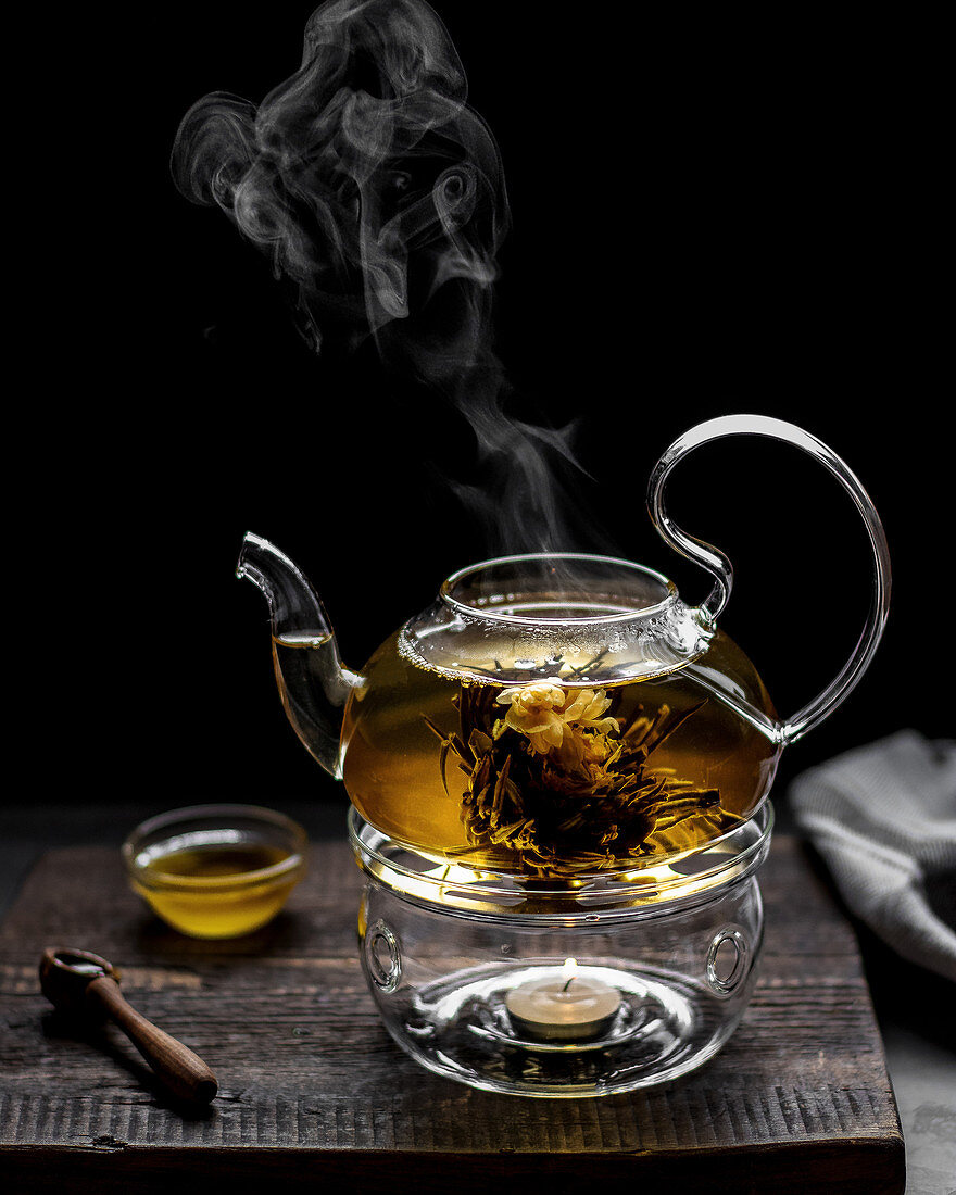 Blossom tea in a glass teapot on a warmer against a black background