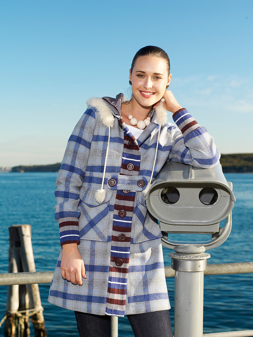 A young woman by the sea wearing a checked coat