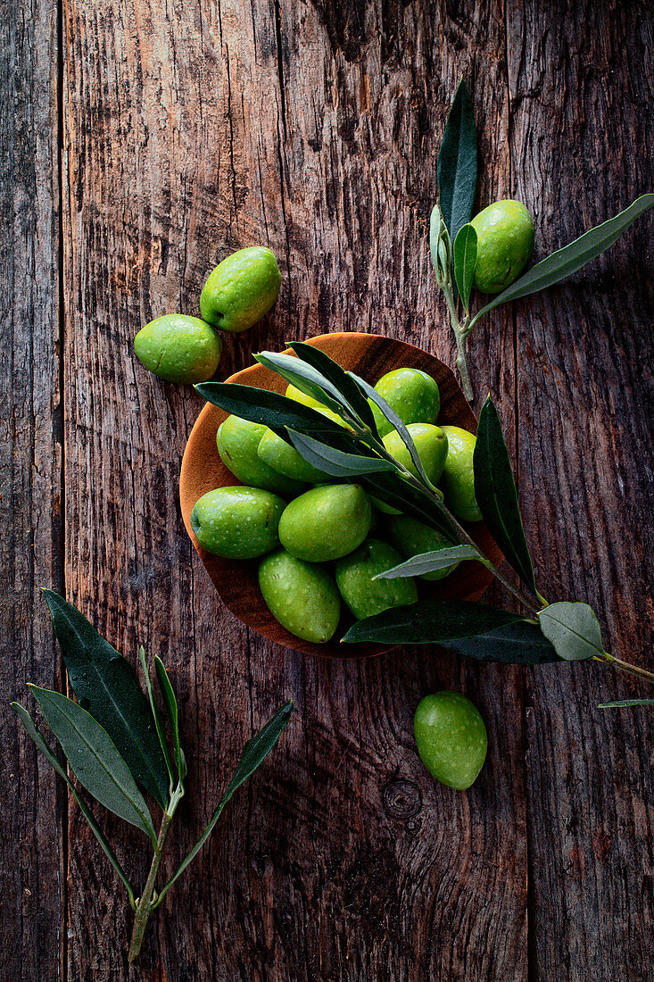 Frische grüne Oliven mit Blättern auf Holzuntergrund