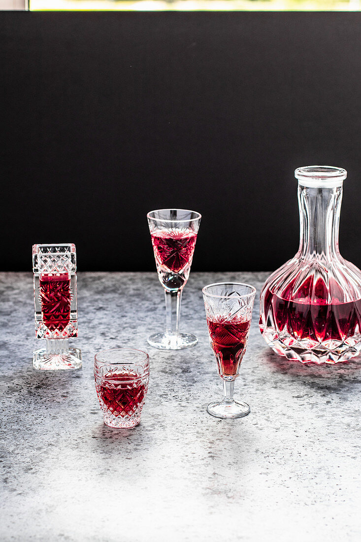 Raspberry liqueur in glasses and a carafe against a black background