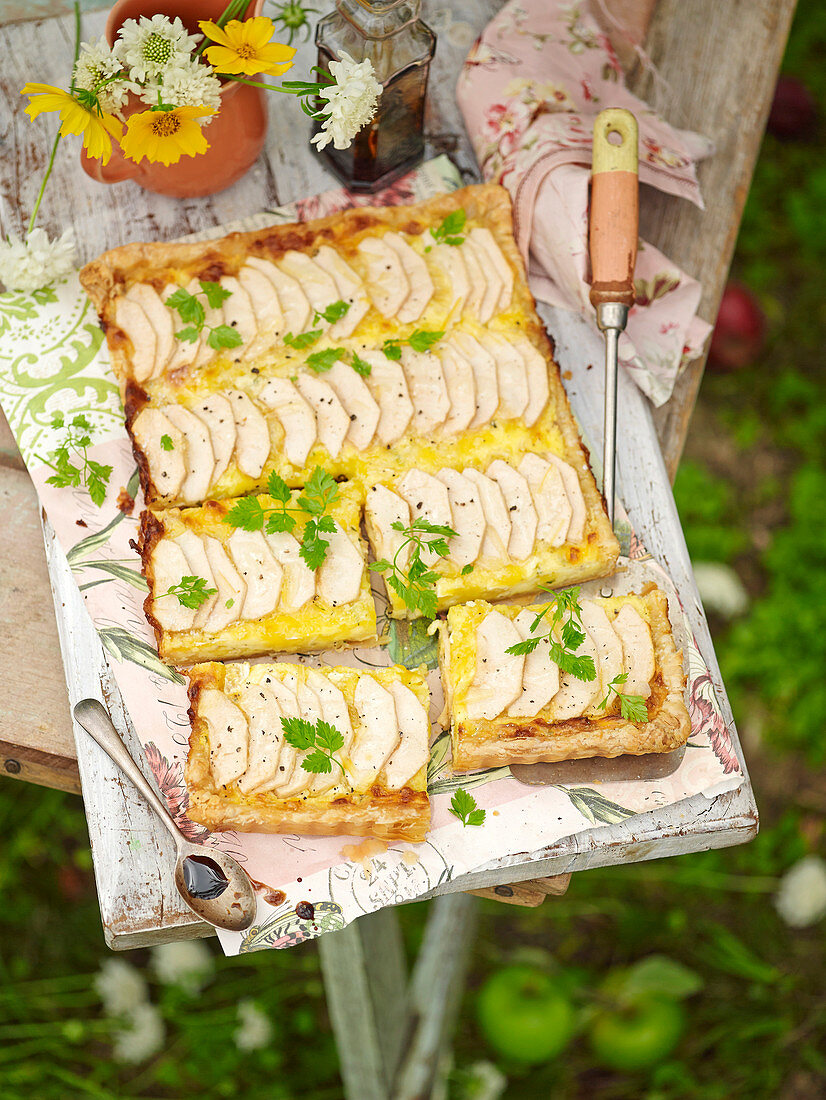 Pikanter Apfelkuchen vom Blech mit Brie auf Tisch im Garten