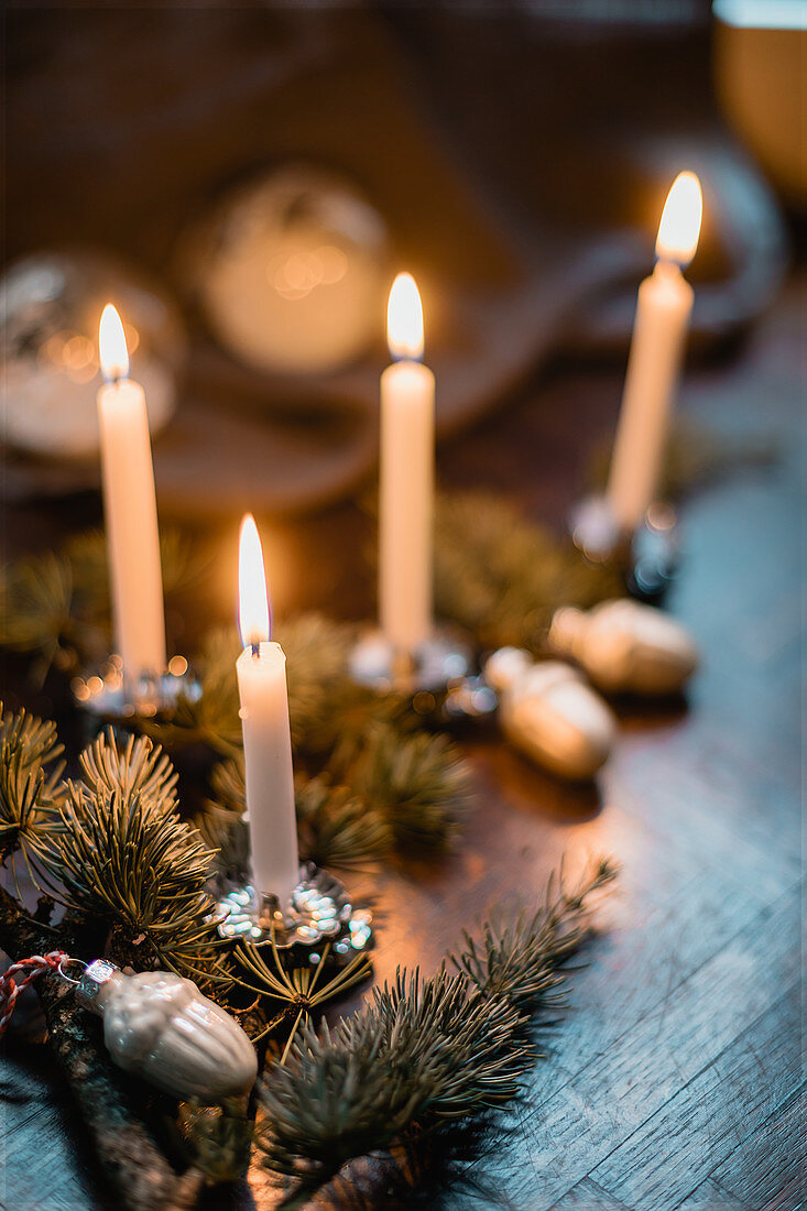 Weihnachtliche Tischdekoration mit Nadelzweigen und brennenden Kerzen