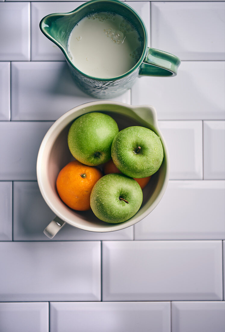 Apples and oranges in ceramic bowl with milk jug