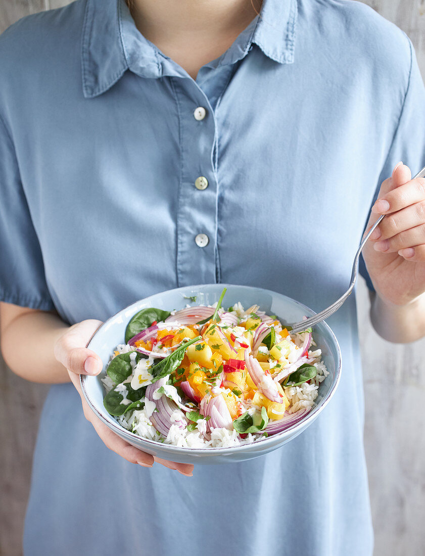 Frau hält Teller mit exotischem Reissalat mit Gemüse und Ananas