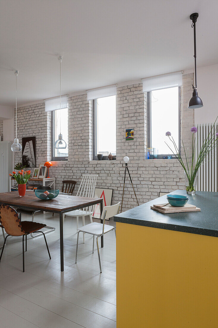 Dining area with various chairs in front of white painted brick wall in open plan living room