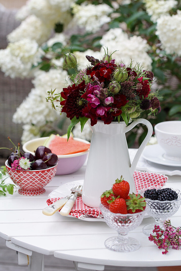Bouquet of red summer flowers and Love-in-a-Mist seed pods and bowls with strawberries, cherries, and blackberries