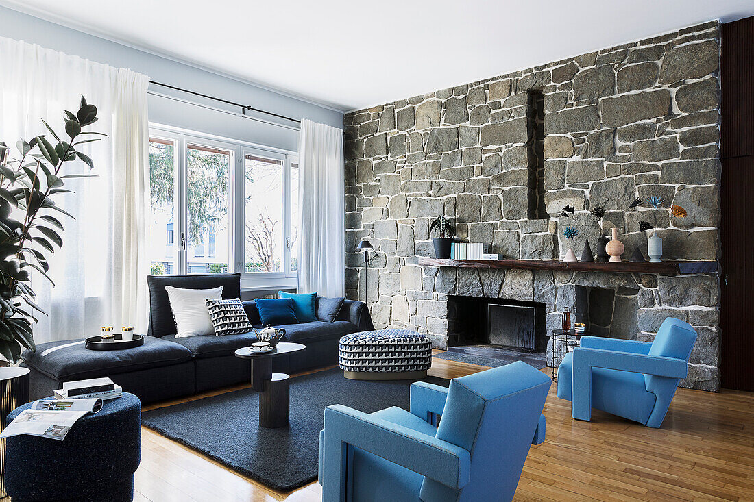 Hellblaue Designersessel und Sofa im Wohnzimmer mit Natursteinwand