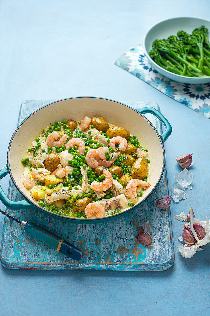 One pot dish of fish and prawns with new potatoes and creamy garlic saucw with fresh peas and broccoli