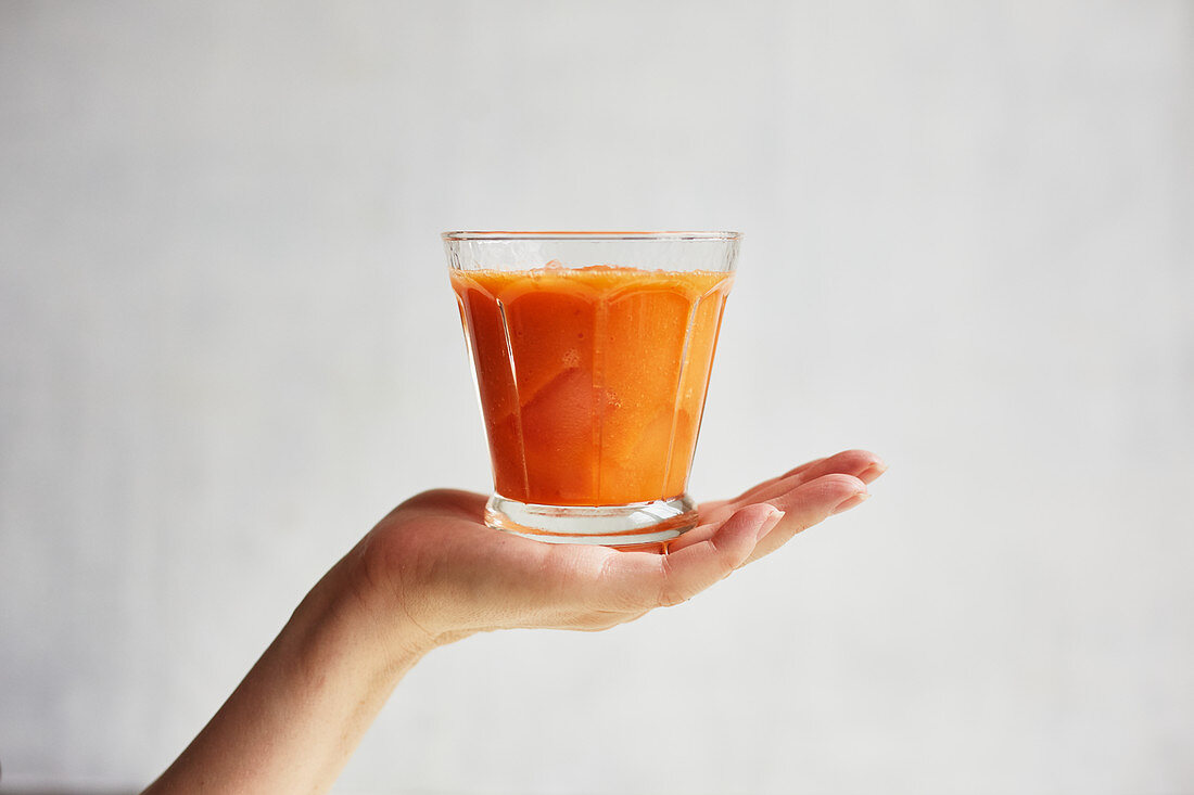 A hand holding a carrot and apple smoothie with ginger