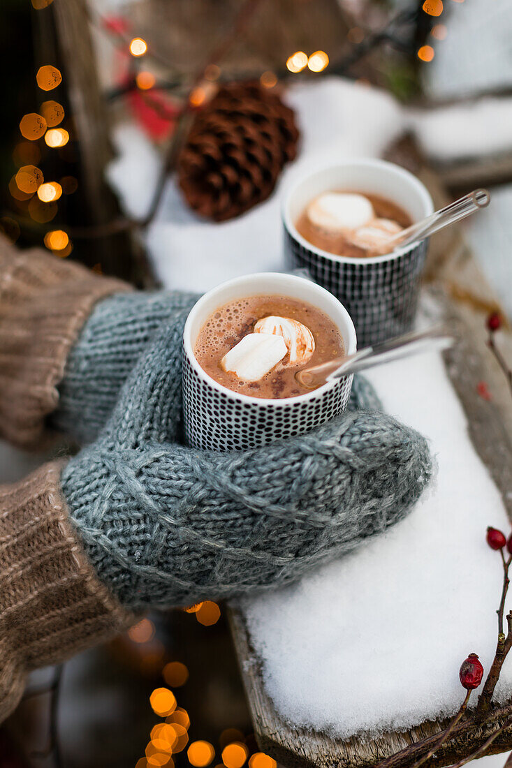 Gloved hands holding hot chocolate with marshmallows