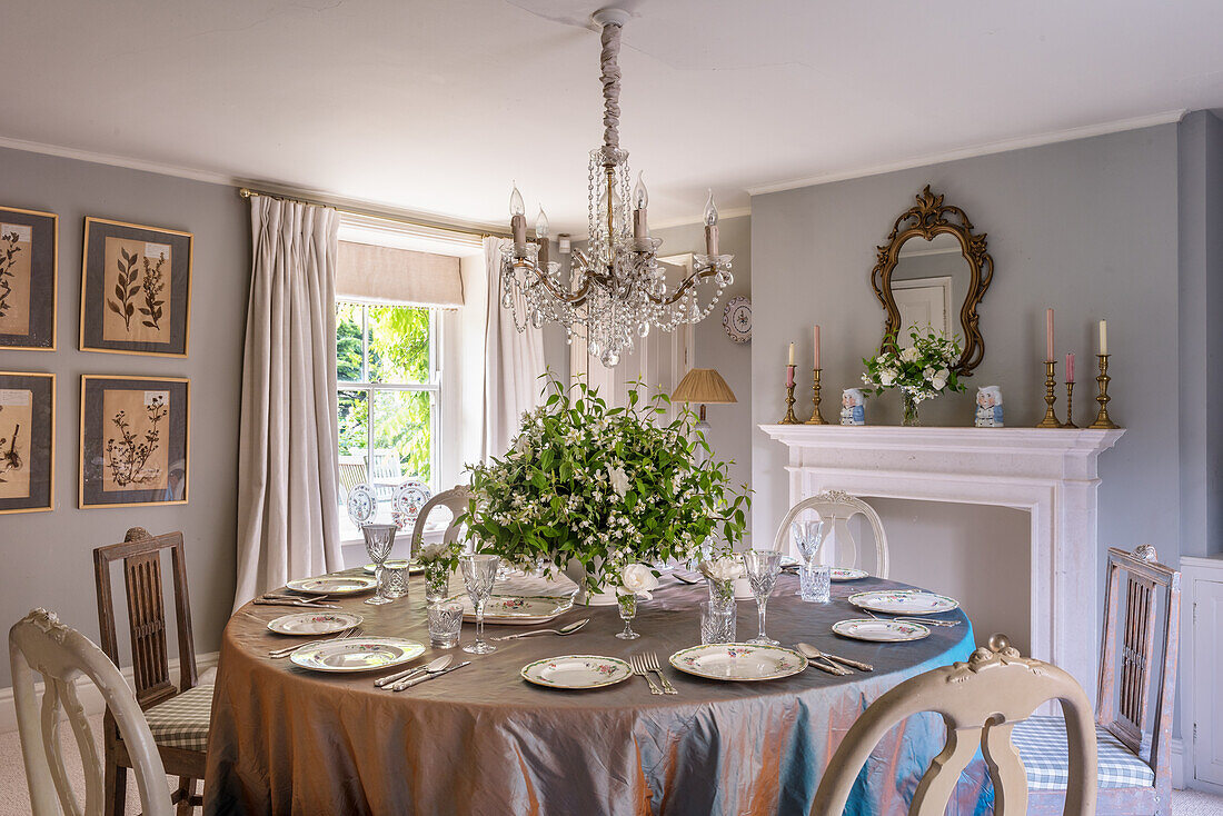 Set, round table below French chandelier next to disused fireplace