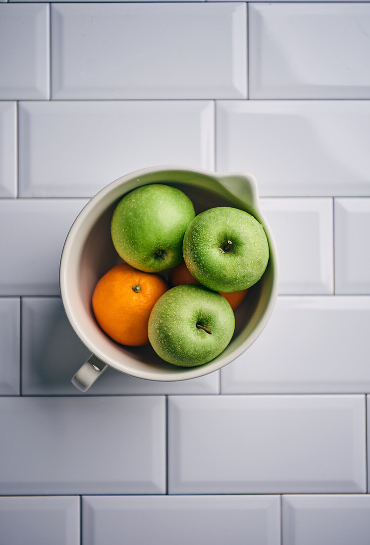 Grüne Äpfel und Orangen in Keramikgefäß