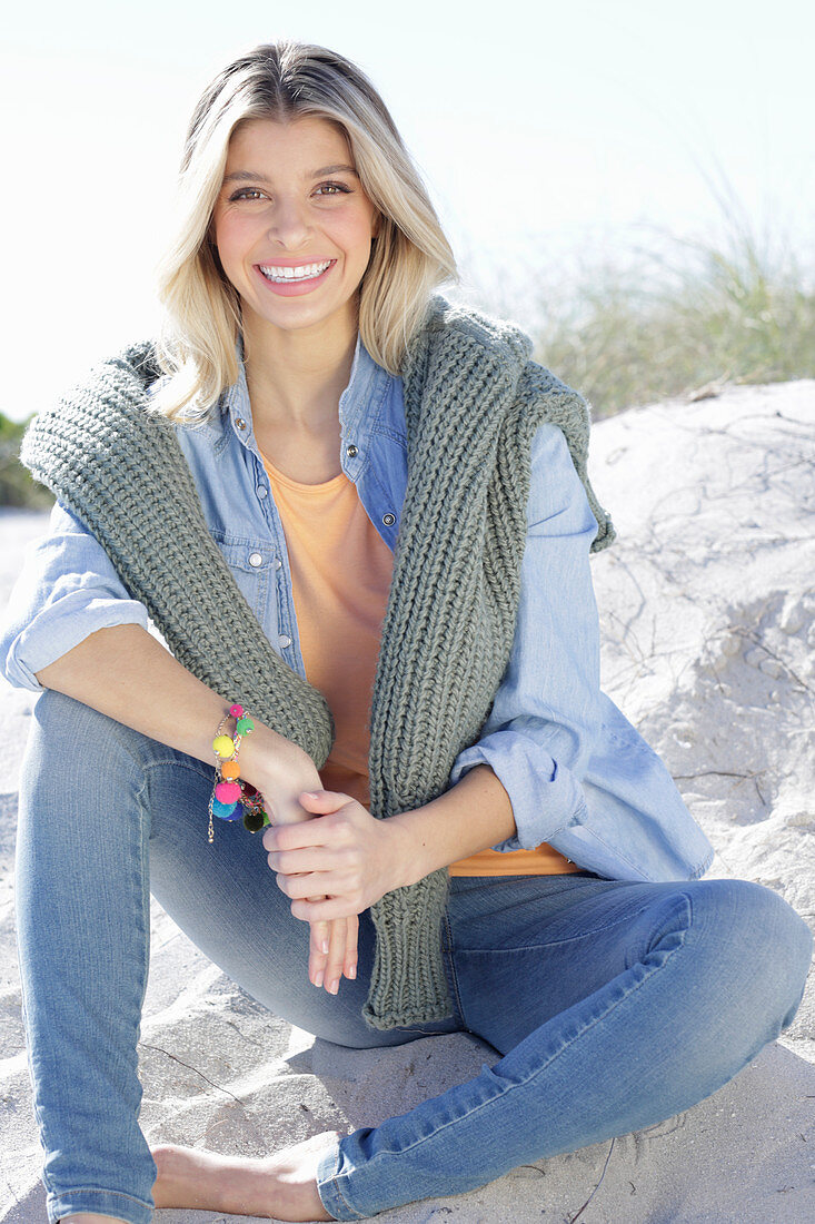 Junge blonde Frau Jeanskleidung und Strickpulli über den Schultern