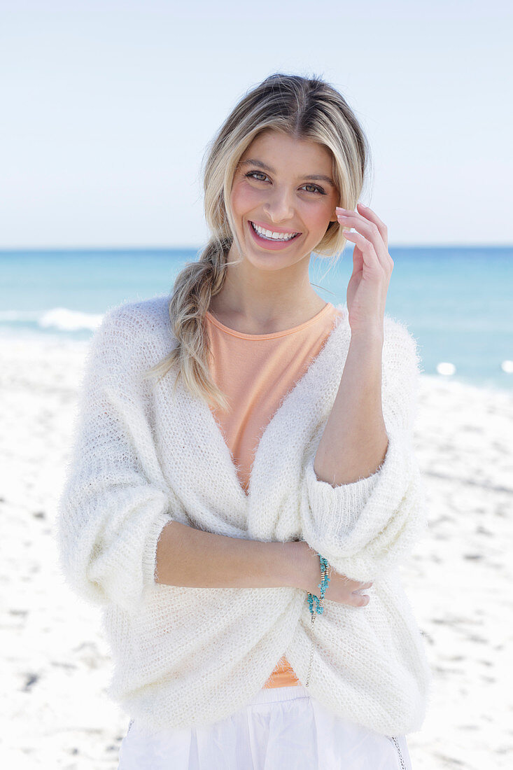 A young blonde woman wearing an apricot top and a white knitted jumper