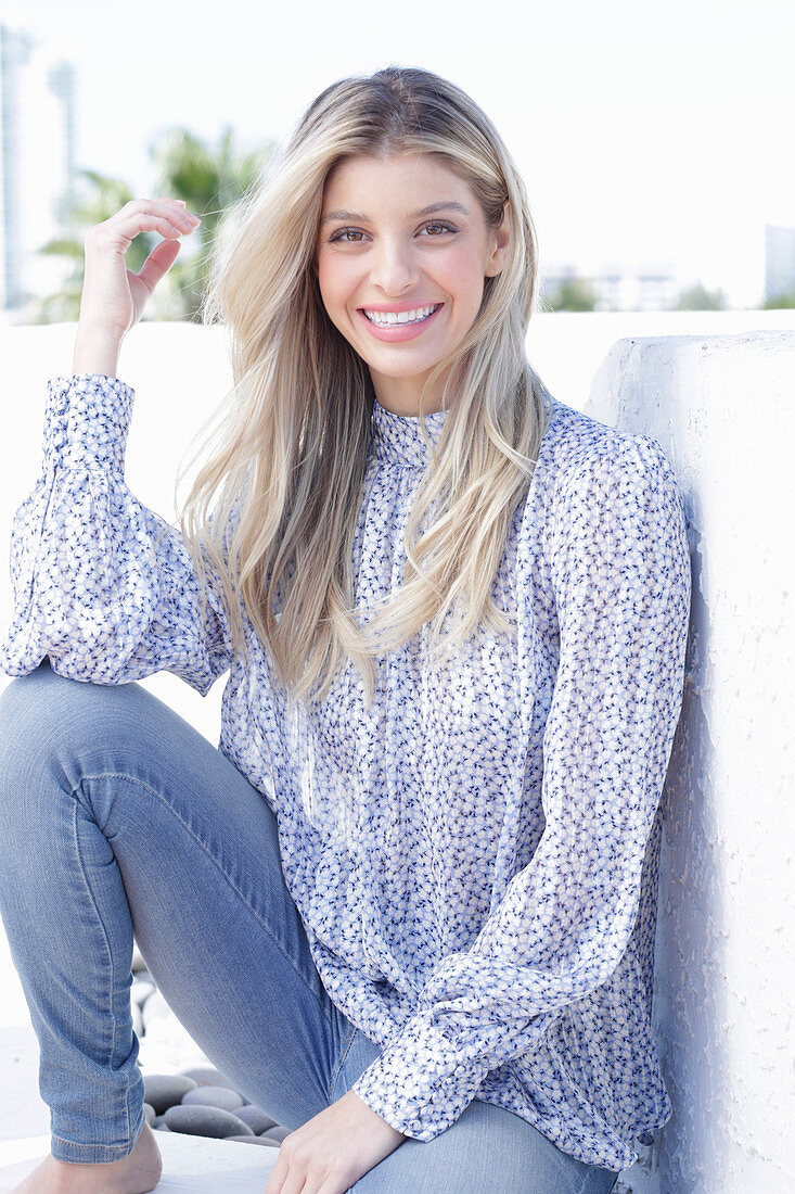 A young blonde woman wearing a blue-and-white patterned top and jeans