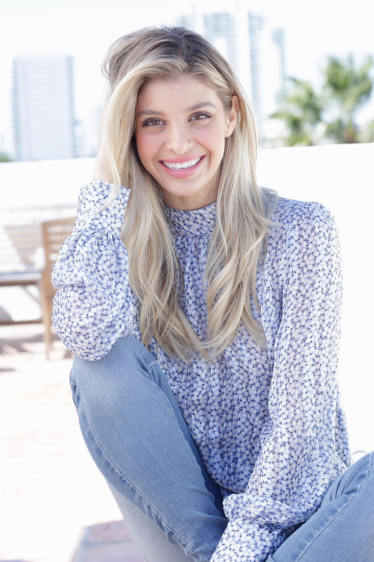 A young blonde woman wearing a blue-and-white patterned top and jeans