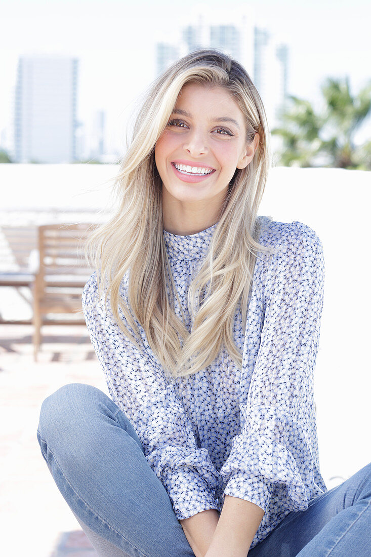 A young blonde woman wearing a blue-and-white patterned top and jeans