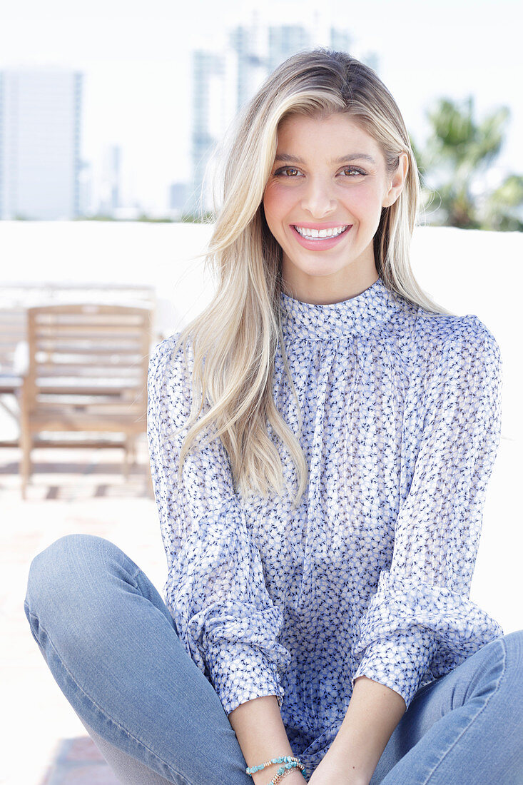 A young blonde woman wearing a blue-and-white patterned top and jeans