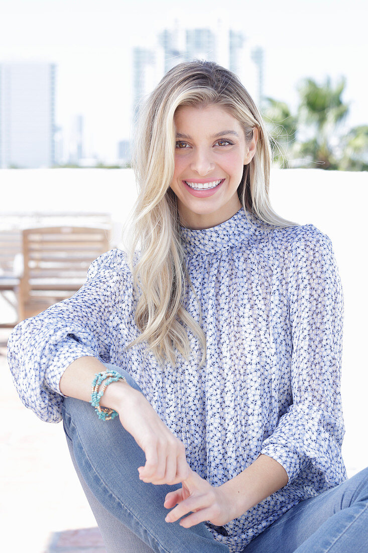 A young blonde woman wearing a blue-and-white patterned top and jeans