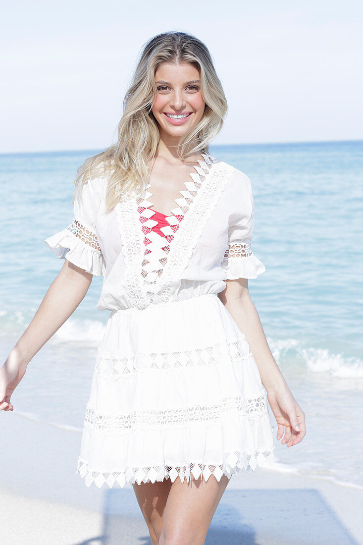 A young blonde woman wearing a white embroidered summer dress