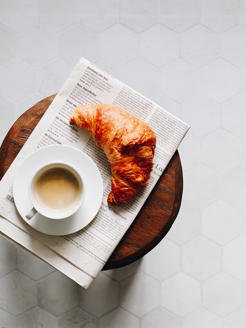 Breakfast croissant, cup of coffee and newspaper on a wooden stool