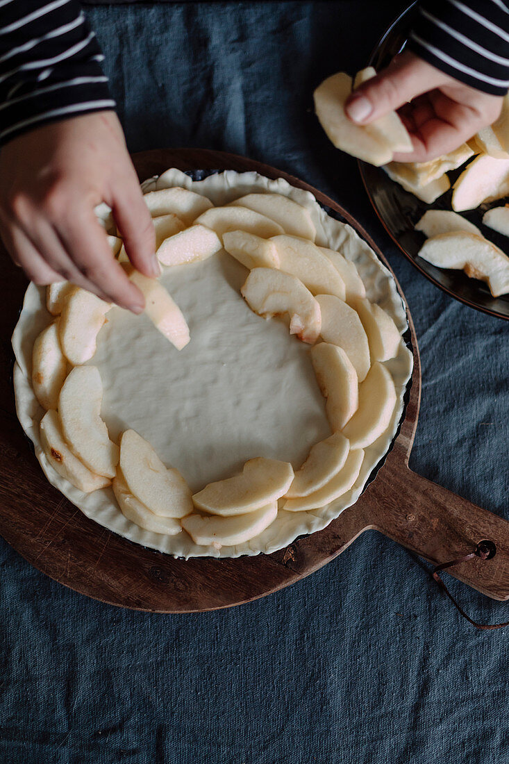 Woman covers an unbaked tart base with apple wedges