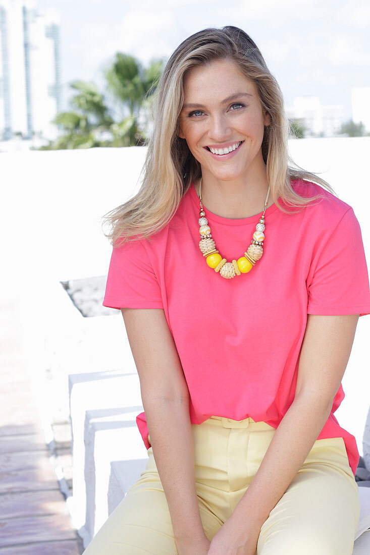 A young blonde woman wearing a pink t-shirt and a pair of light trousers