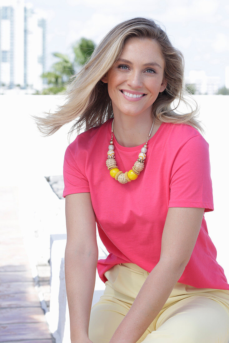 A young blonde woman wearing a pink t-shirt and a pair of light trousers