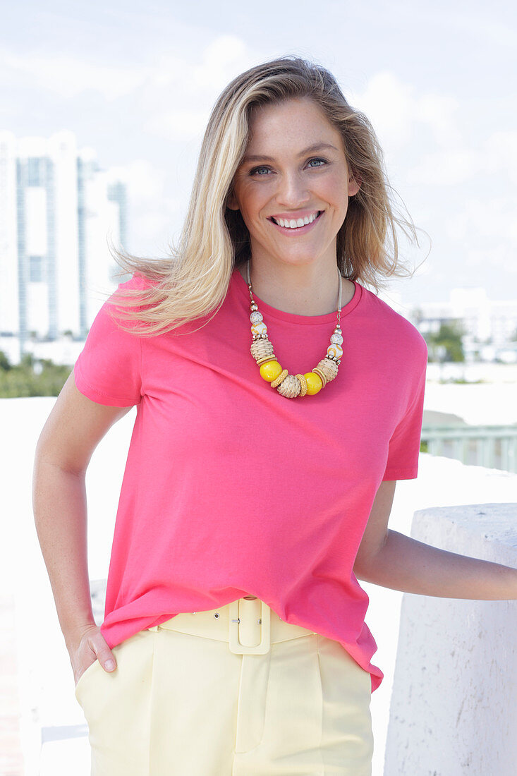 A young blonde woman wearing a pink t-shirt and a pair of light trousers
