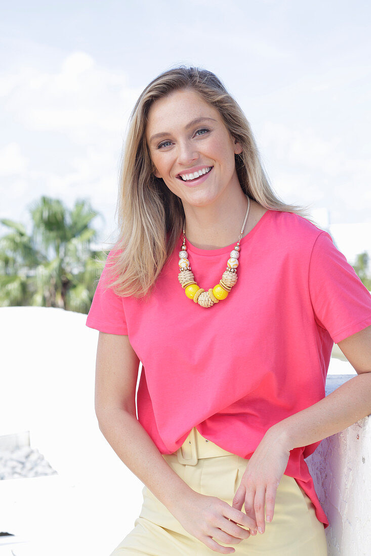 A young blonde woman wearing a pink t-shirt and a pair of light trousers