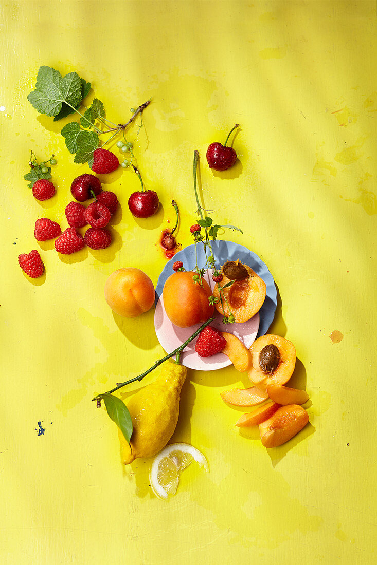 Lemons, apricots and fresh berries on a yellow background