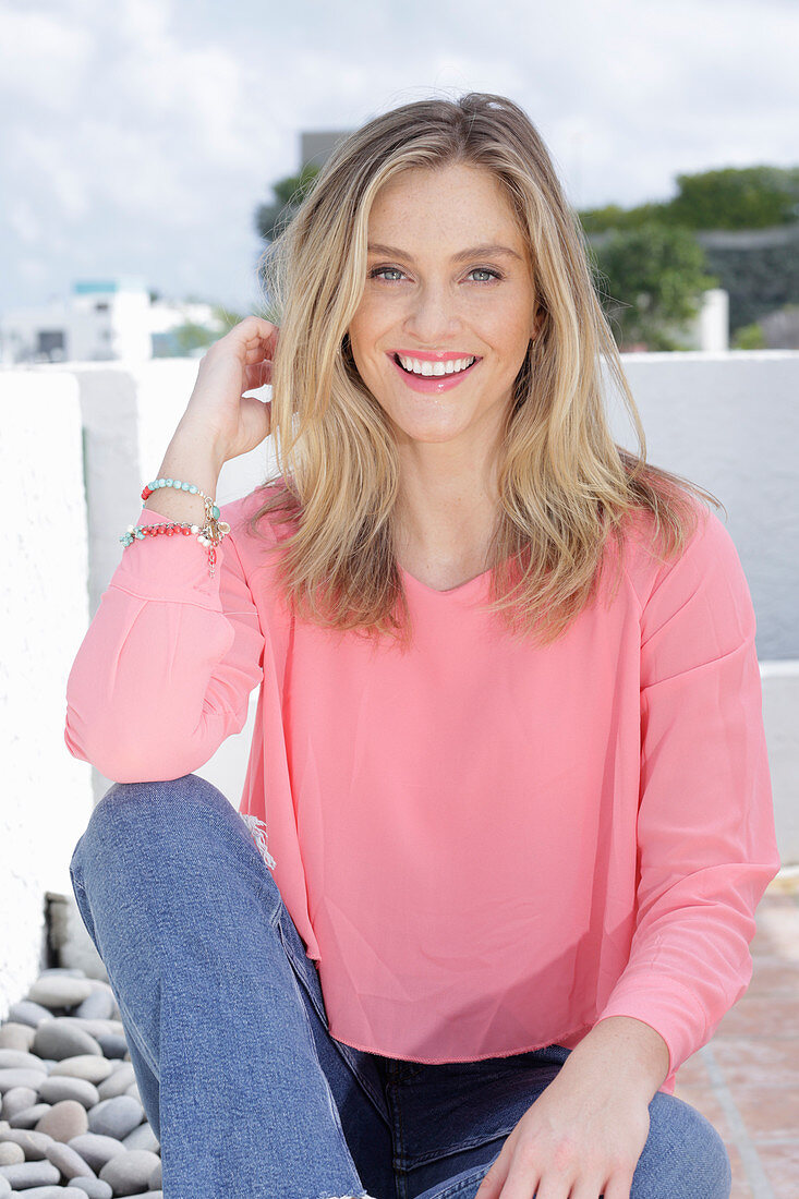 A young blonde woman wearing a pink top and jeans