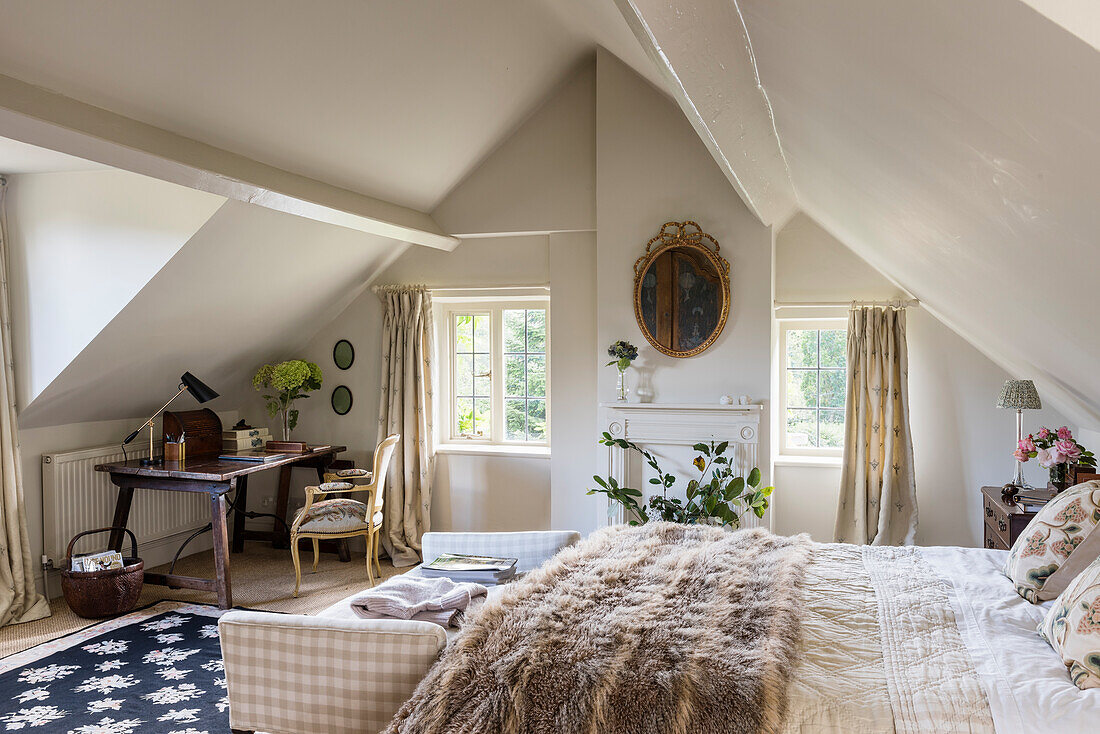 Desk and chair in attic with gilt framed artwork and double bed with fur throw