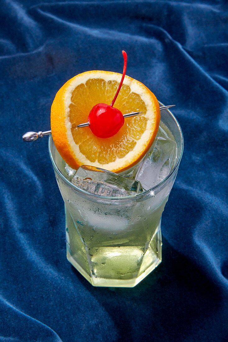 Ein Tom Collins mit Eiswürfeln, Orangenscheibe und Cocktailkirsche