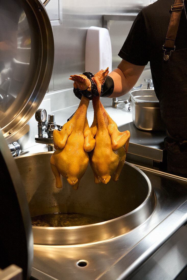 Koch gibt Hähnchen in Fritteuse (China)
