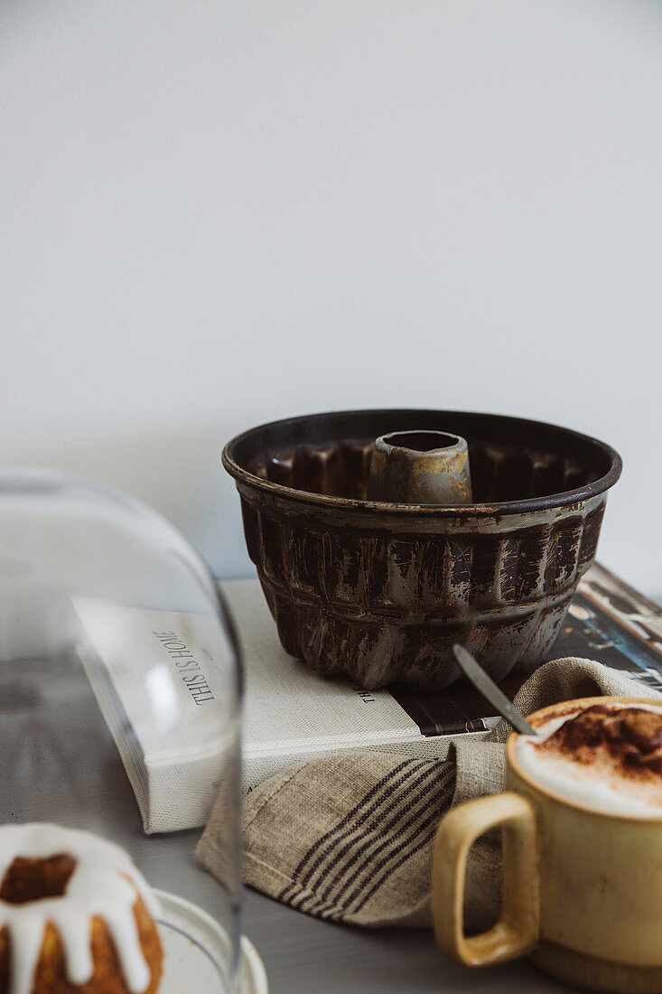 Antike Guglhupf-Backform, Cappuccino und Minikuchen unter Glashaube