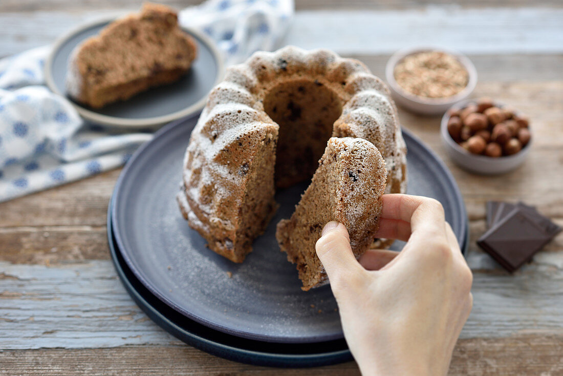 Vegan hazelnut chocolate bundt cake - a woman reaches for a slice of cake