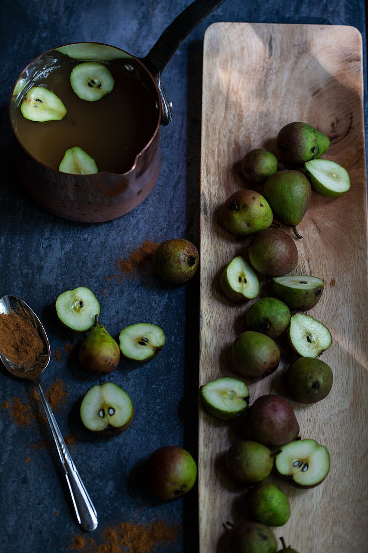 Small seckel pears, halved and whole, in a wooden tray, with a copper pot of apple cider and cinnamon