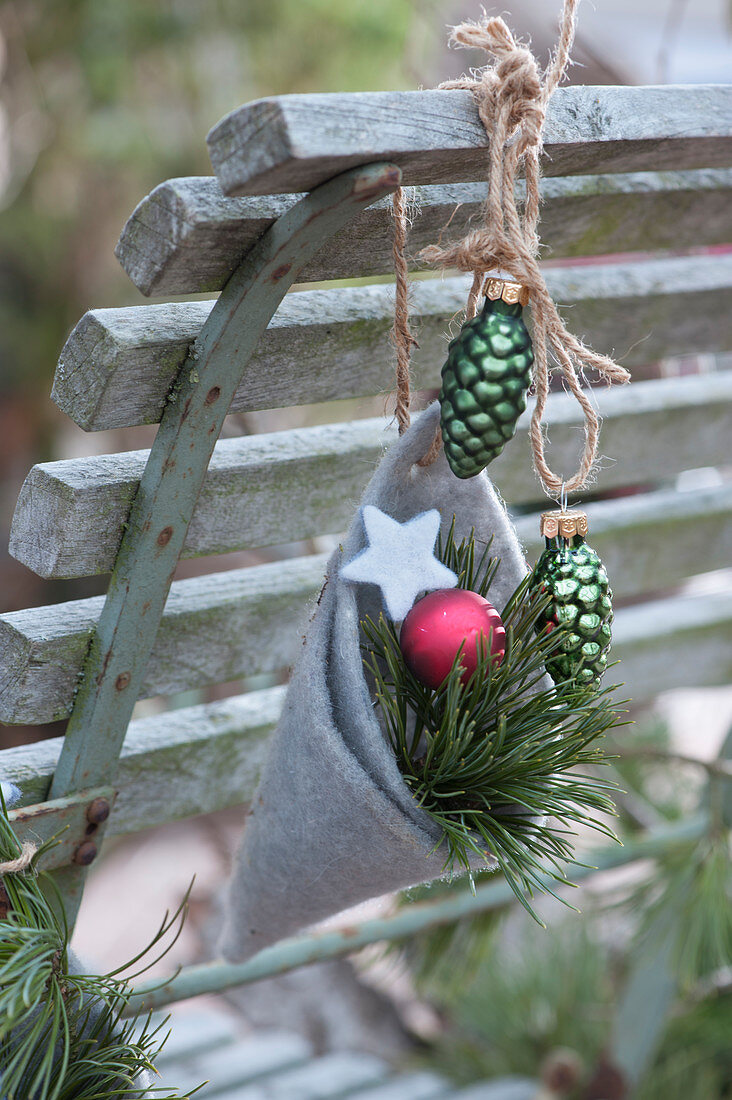 Homemade felt bag with Christmas tree decorations and pine branch hung on the back of a chair