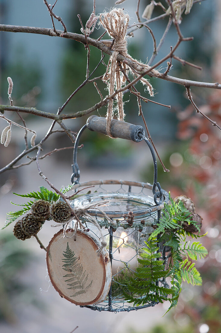 Hanging lantern with a self-made pendant made from a wooden disc, cones and fern leaves