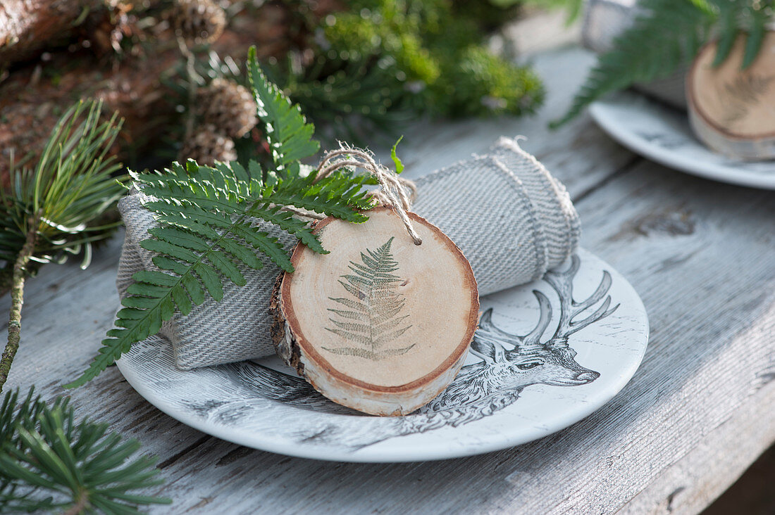 Selbstgemachter Anhänger aus Holzscheibe mit Farnblatt als Serviettendekoration