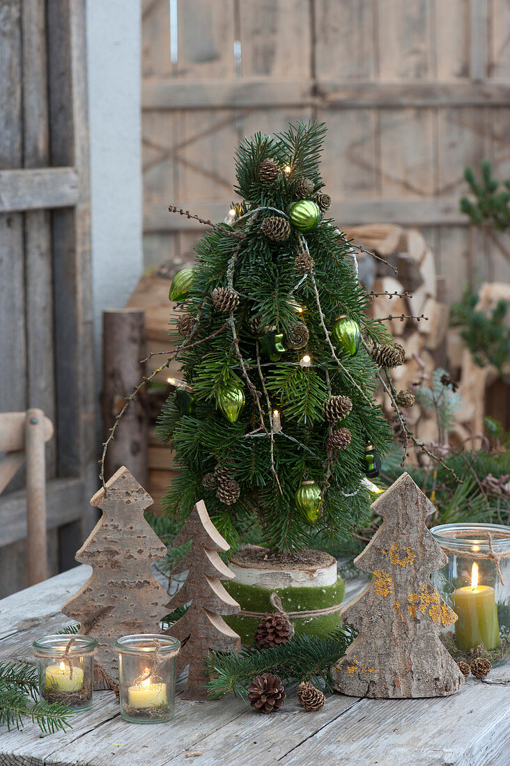 A tied tree made of fir branches in a wooden disc, decorated with Christmas tree decorations and pinecones, wooden fir trees and lanterns