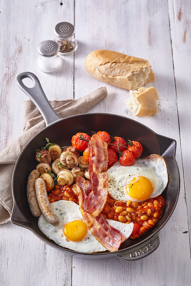 Englisches Frühstück mit Bohnen, Eiern, Würstchen und Speck in der Pfanne