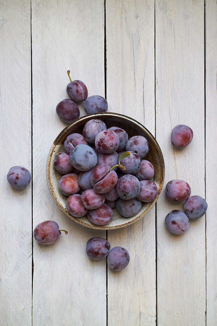 A dish of ripe plums against a white wood background