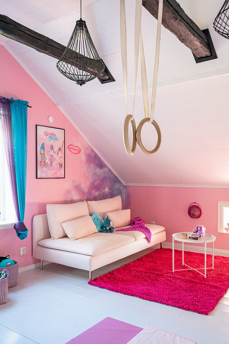 Bright upholstered sofa and gymnastic rings hung in the attic room with a pink painted wall