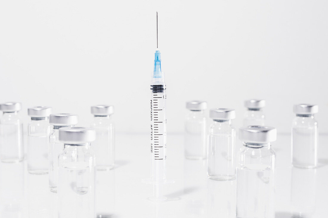 COVID-19 vaccine vials surrounding syringe on white background