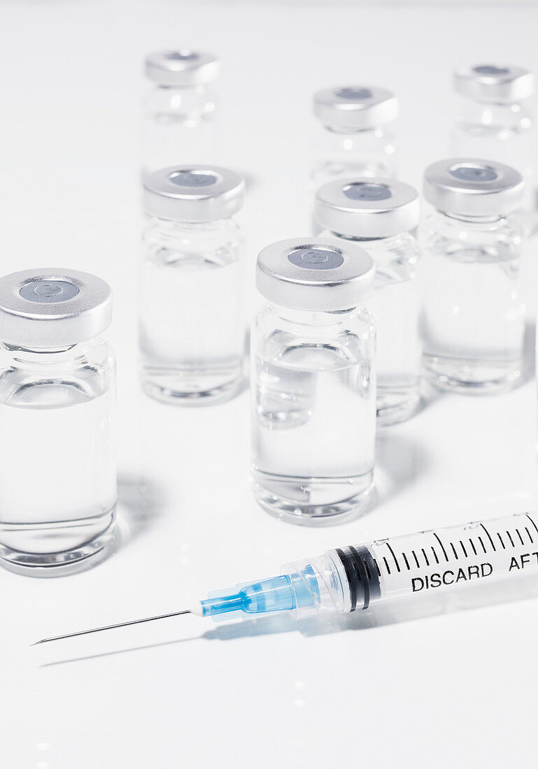 COVID-19 vaccine vials and syringe on white surface