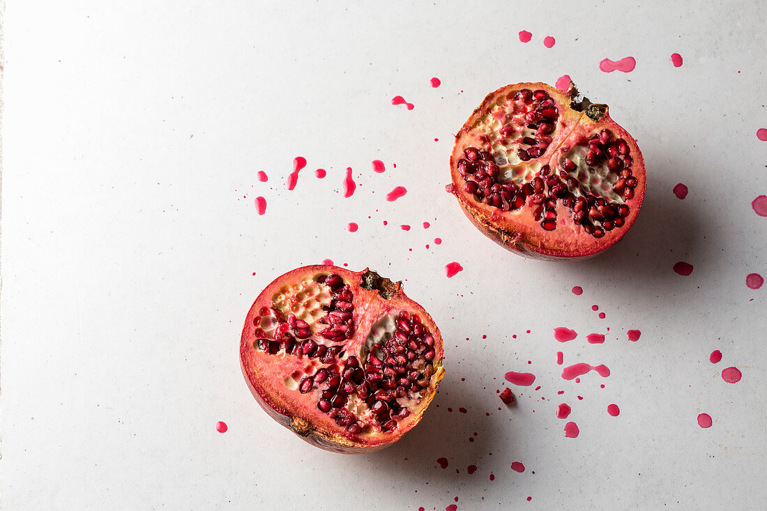 Halbierter Granatapfel mit Saftspritzern auf weißem Untergrund