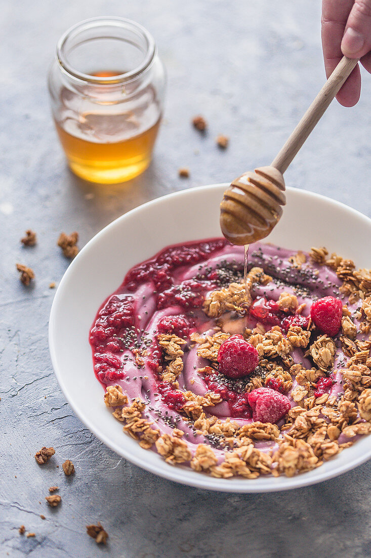 Drizzling honey over granola with yoghurt, raspberry and chia seeds