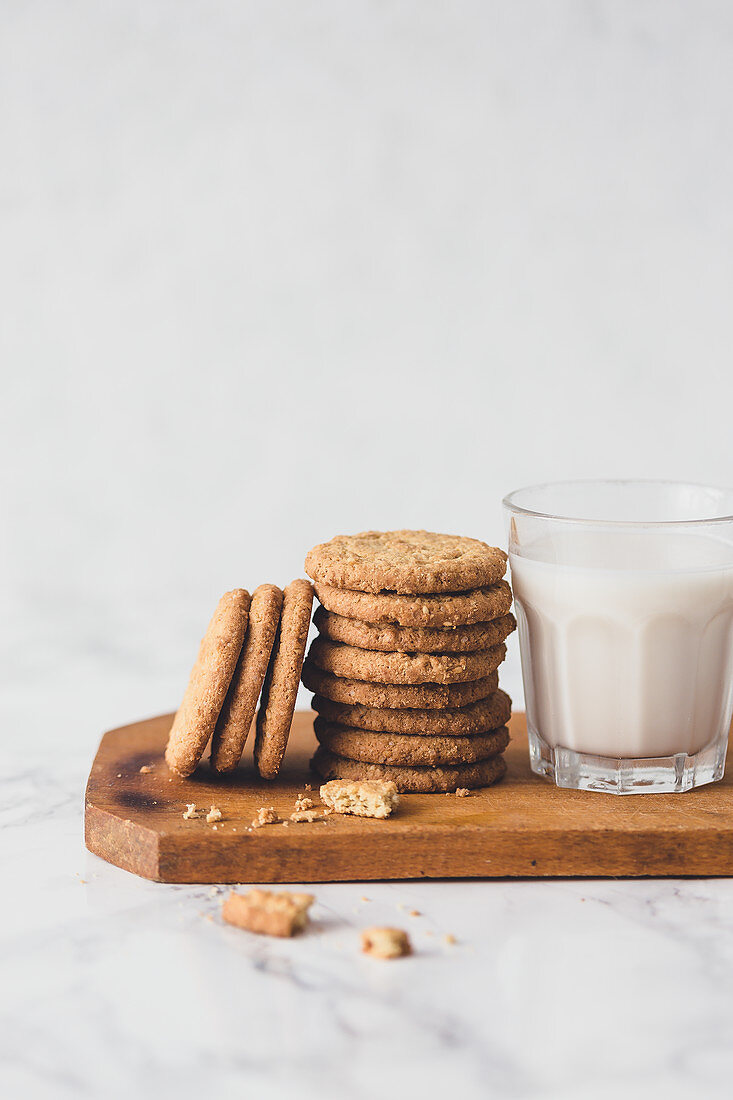 Cookies und ein Glas Milch auf Holzbrett vor hellen Hintergrund
